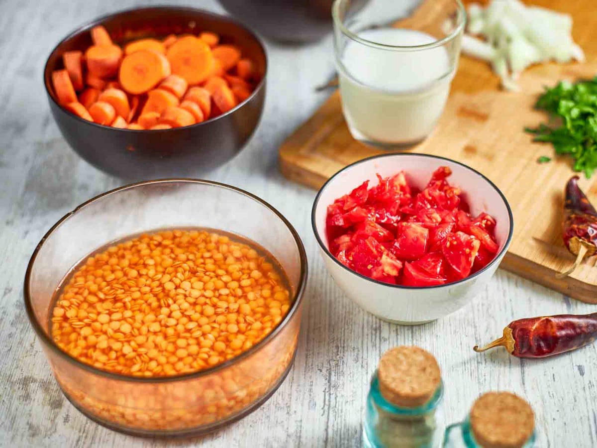 Chopped carrots, tomatoes, and soaked red lentils are prepped alongside spices and herbs, ready for cooking a hearty soup.