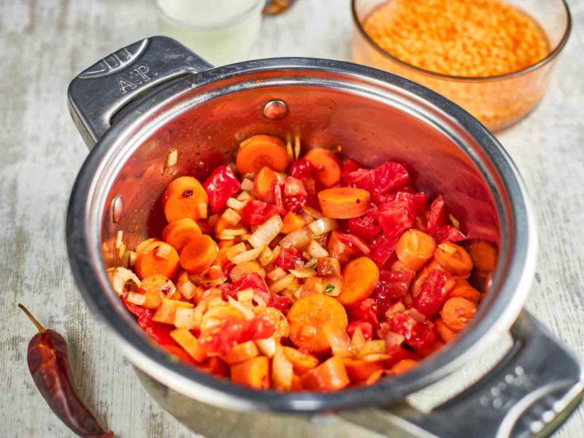 Chopped carrots, tomatoes, and onions are sautéing together, building the base for a rich and flavorful soup.