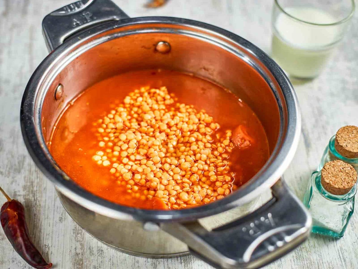 Red lentils are added to the pot with the sautéed vegetables and liquid, ready to simmer into a hearty soup.
