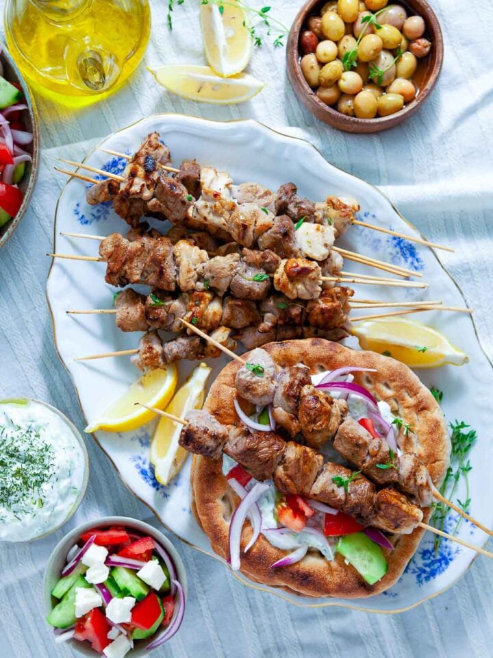 Grilled souvlaki skewers with pita, tzatziki, olives, and salad