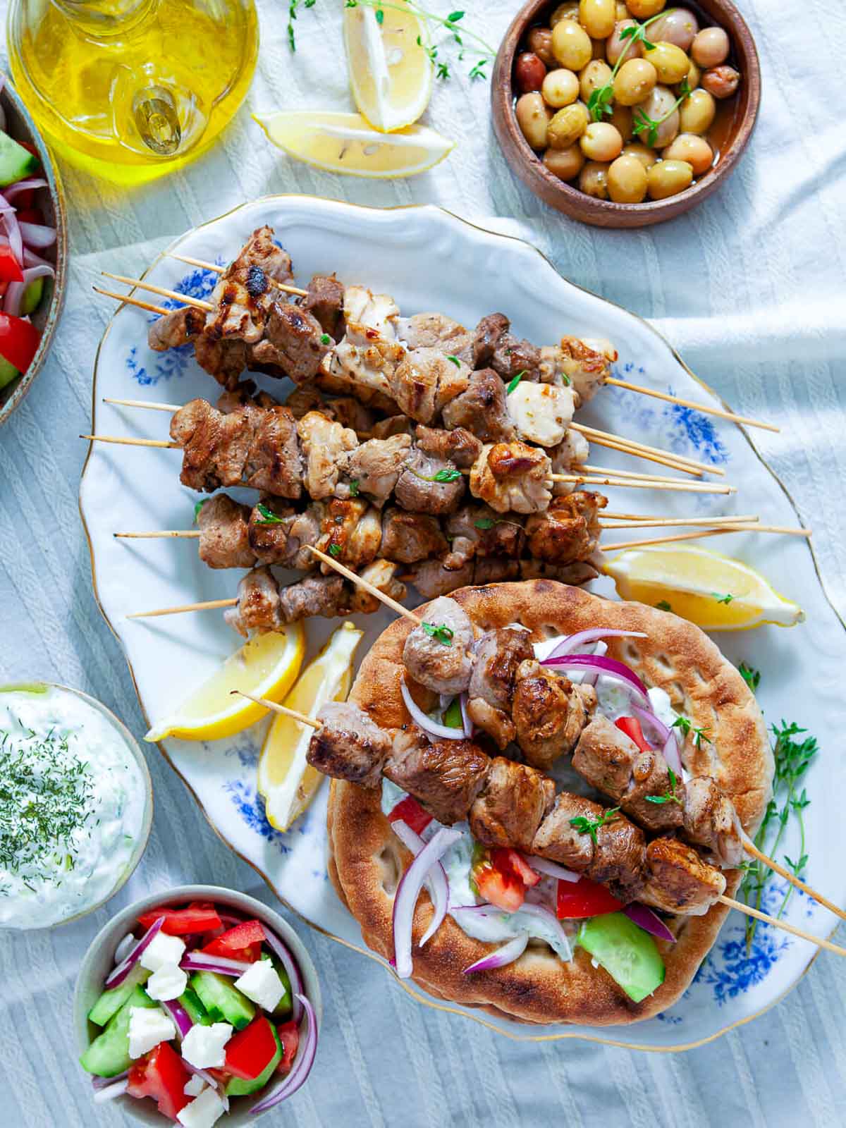 Grilled souvlaki skewers with pita, tzatziki, olives, and salad