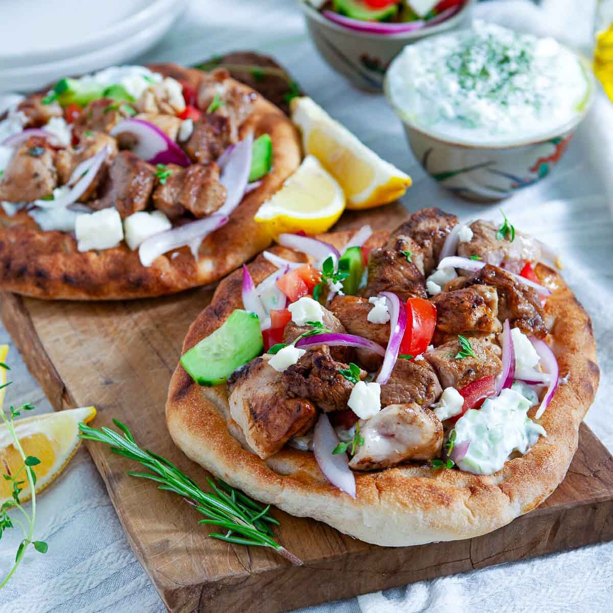 Grilled meat skewers served on warm flatbread, topped with fresh vegetables and tzatziki sauce, ready to eat