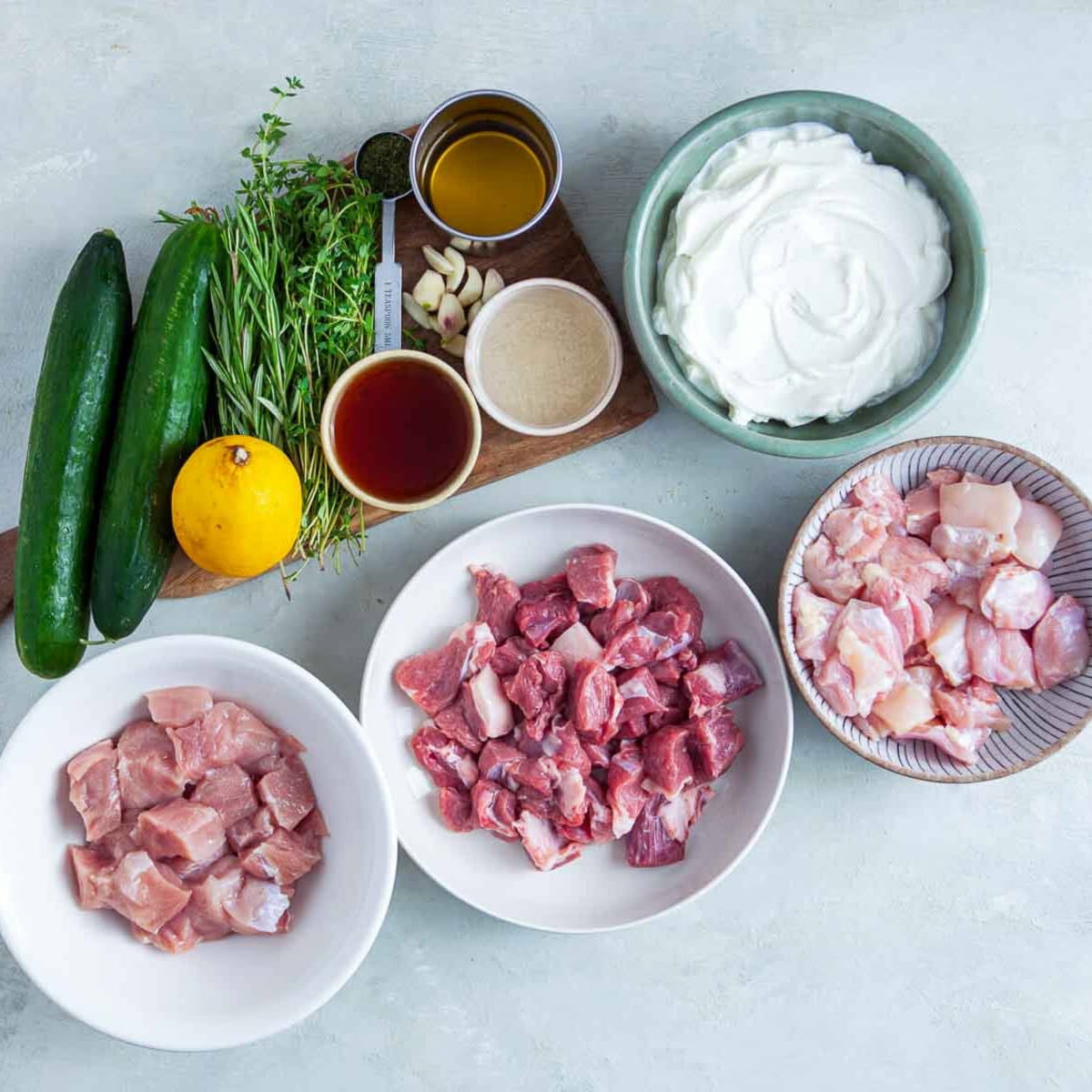 Souvlaki ingredients with meats, yogurt, herbs, cucumbers, and lemon