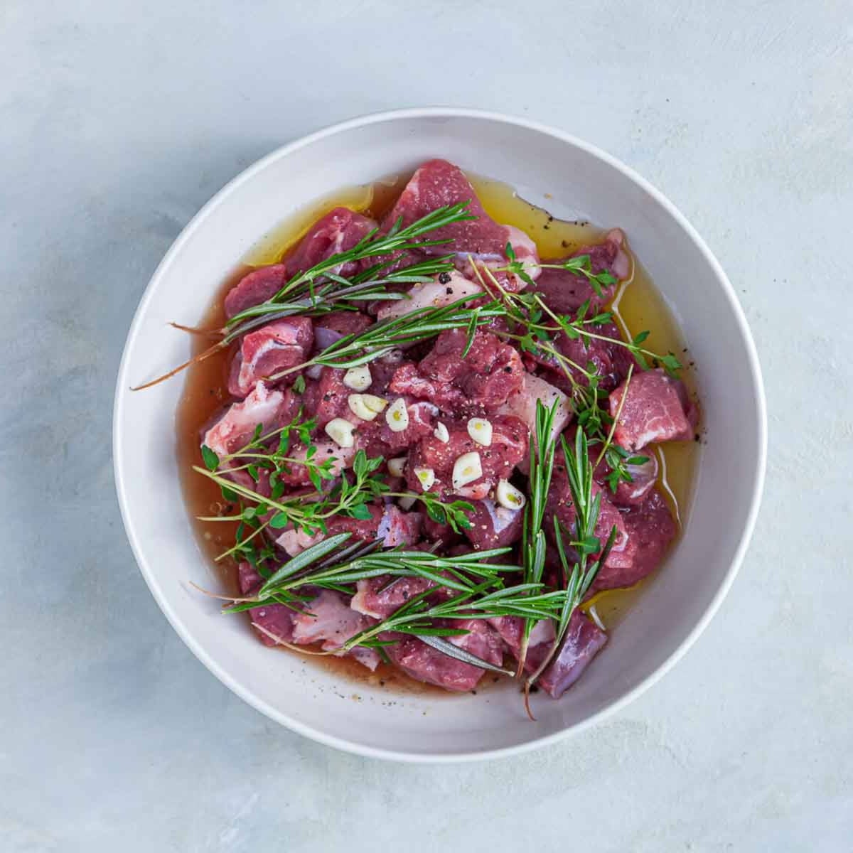 Raw marinated meat with herbs and garlic in bowl