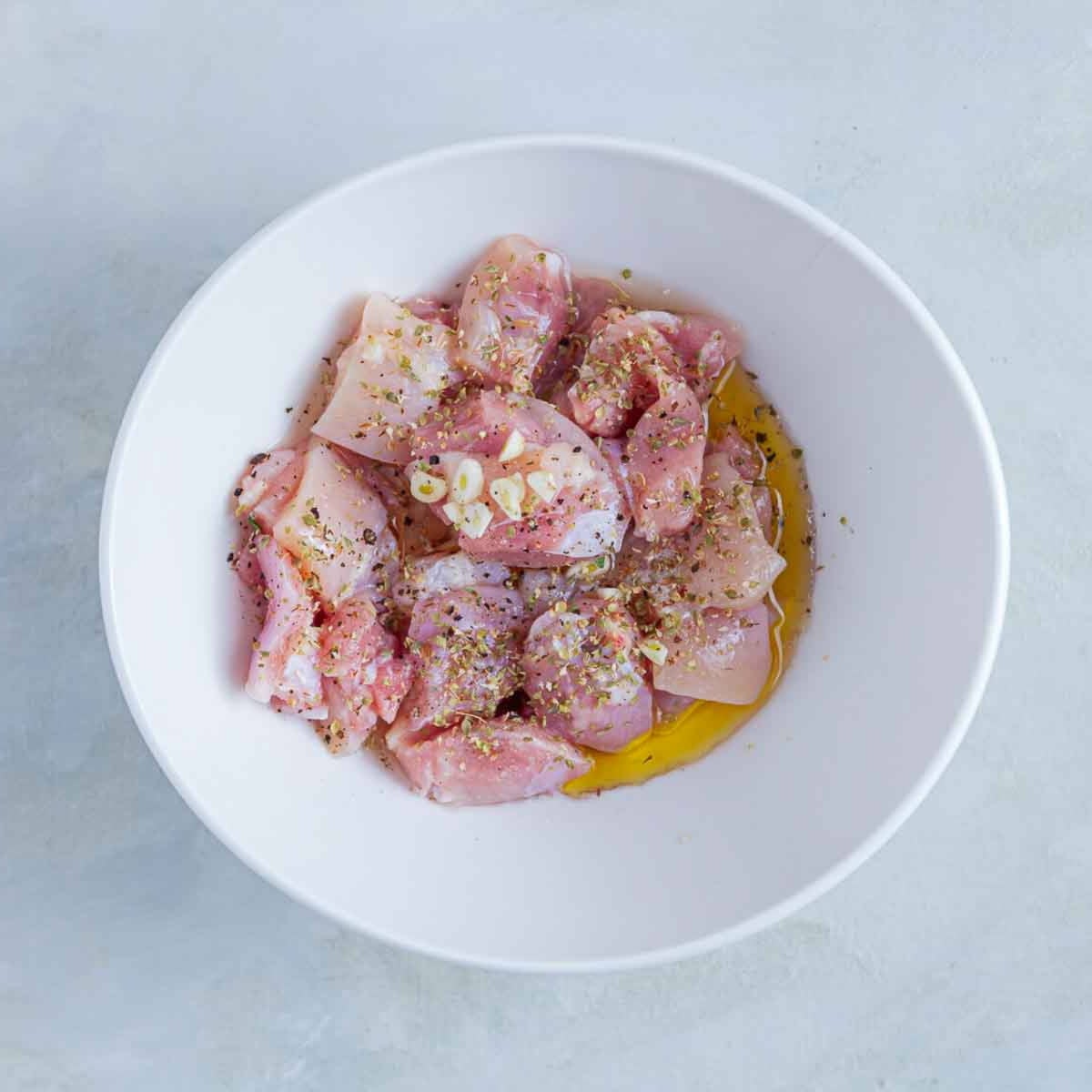 Raw chicken pieces marinating with oil, garlic, and spices