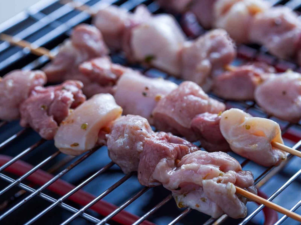 Skewered pieces of marinated meat placed on a grill, beginning to cook over heat
