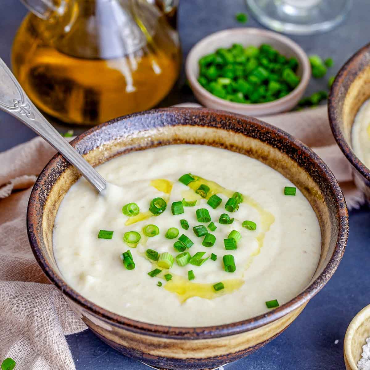 A close-up of a creamy soup garnished with chopped green onions and a drizzle of olive oil, served in a rustic bowl