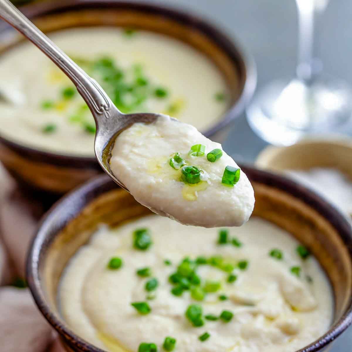 A spoonful of potato leek soup held over the bowl.