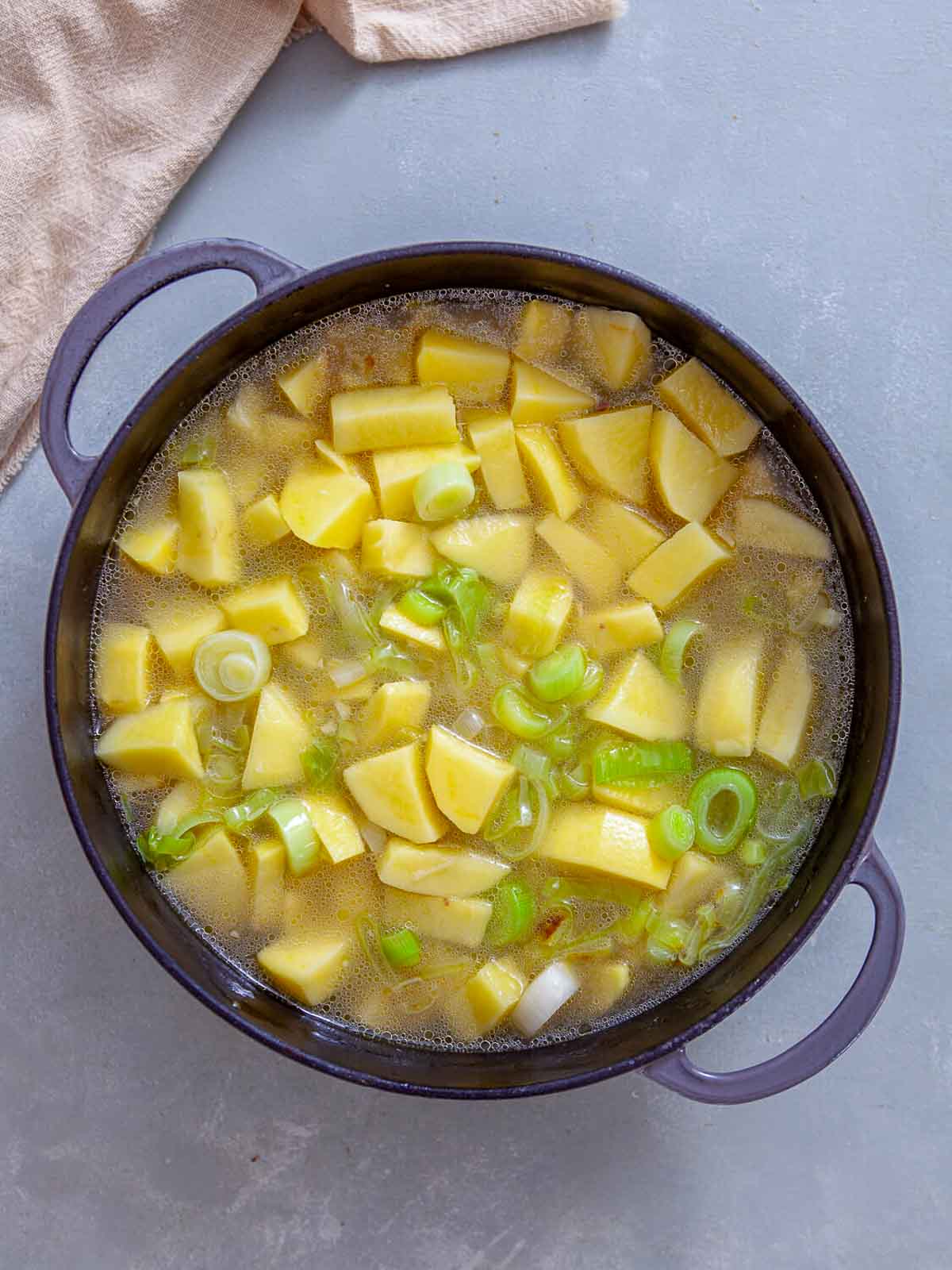 A pot filled with chopped potatoes and sliced leeks simmering in broth, starting to cook into a soup