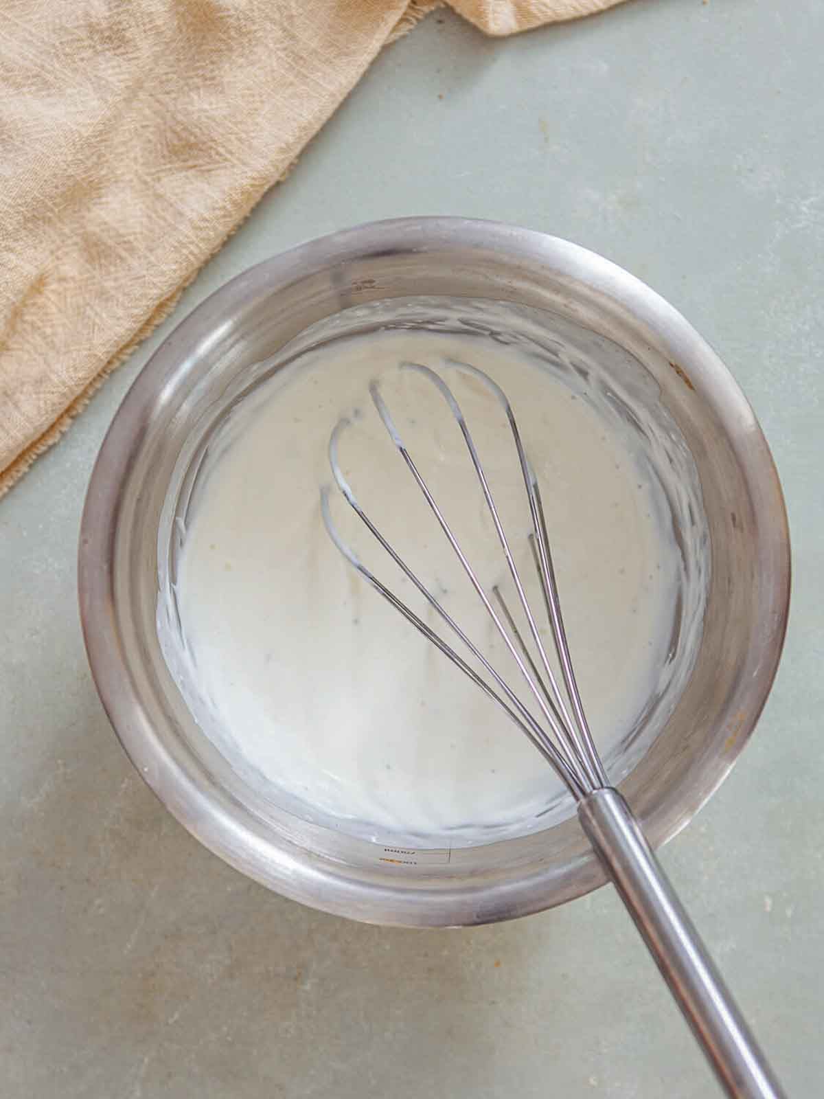 A metal mixing bowl with a whisk stirring a smooth, creamy mixture—likely cream being incorporated to finish the soup’s silky texture