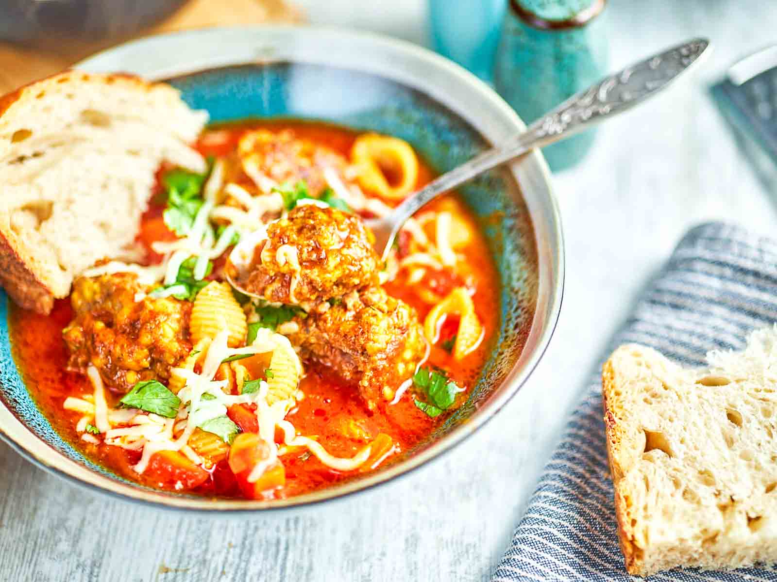 Spoon lifting meatballs from Italian soup with pasta and cheese