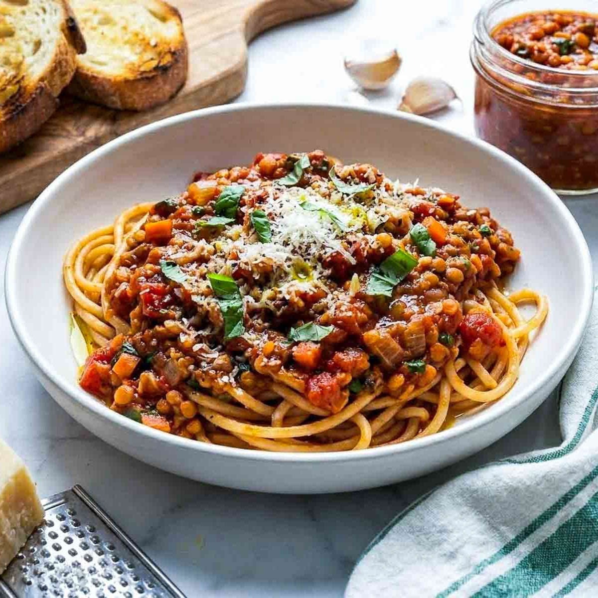 Angled view of a bowl of spaghetti topped with thick red lentil Bolognese sauce, grated Parmesan, and fresh basil.