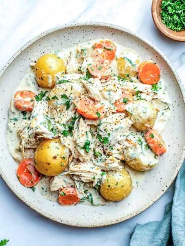 Creamy ranch chicken with cottage cheese served on a plate with baby potatoes and carrots, garnished with parsley and black pepper.