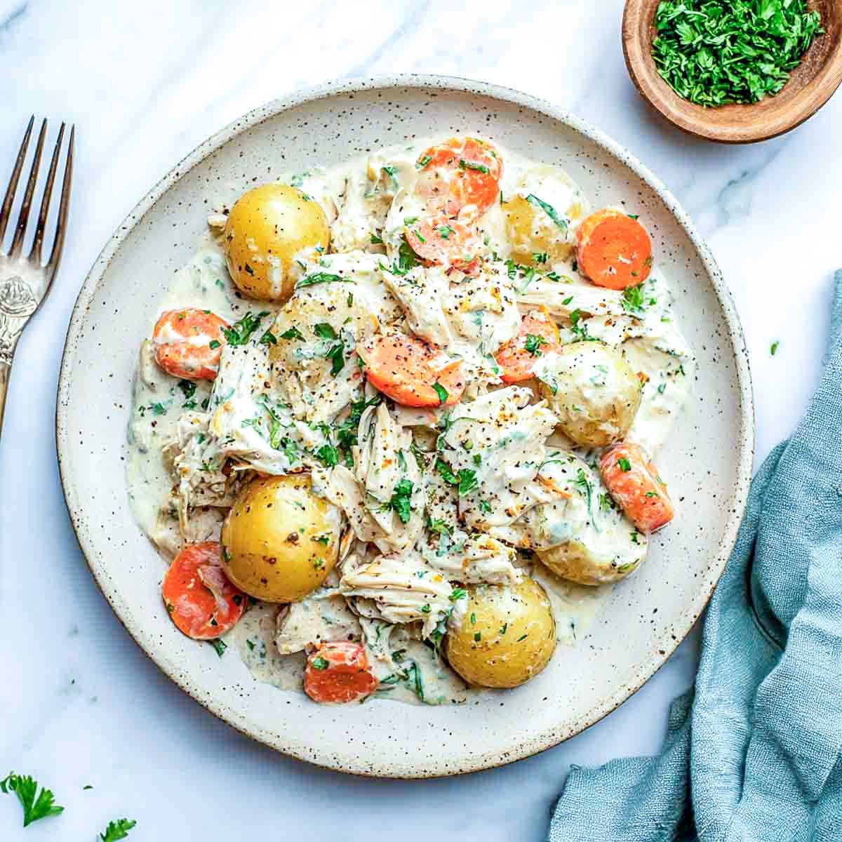 Creamy ranch chicken with cottage cheese served on a plate with baby potatoes and carrots, garnished with parsley and black pepper.