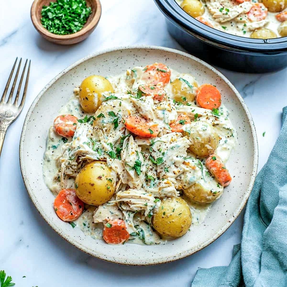 Serving of easy crockpot ranch chicken and potatoes with creamy cottage cheese ranch sauce, with the slow cooker visible in the background.